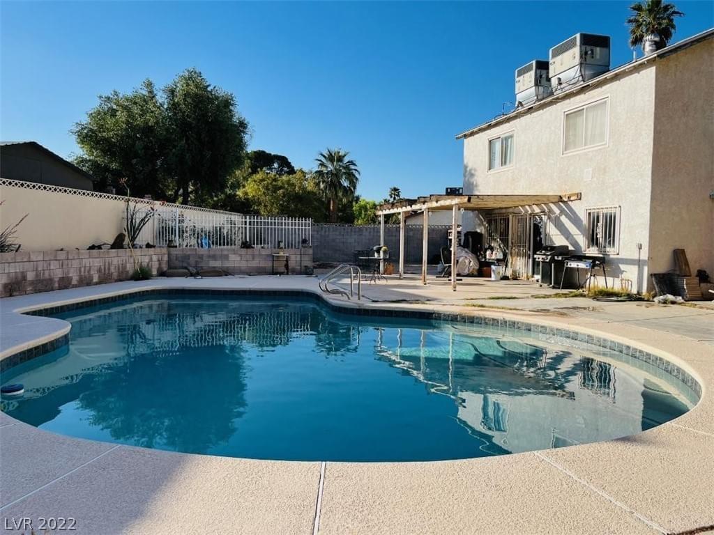 A light gray stucco home with central air units on the roof, covered patio, dark teal pool